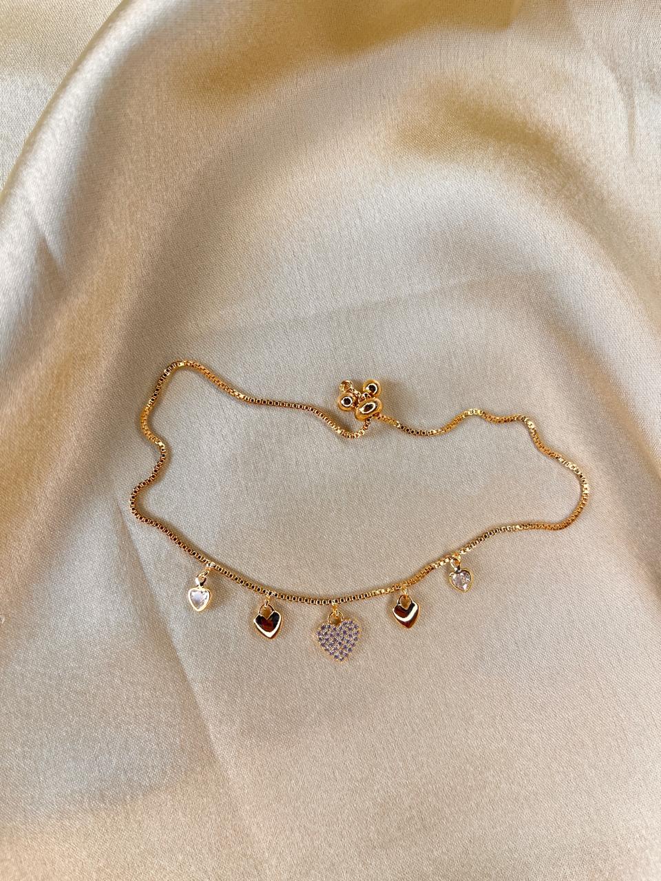 Gold anklet with heart and star charms on a beige fabric background