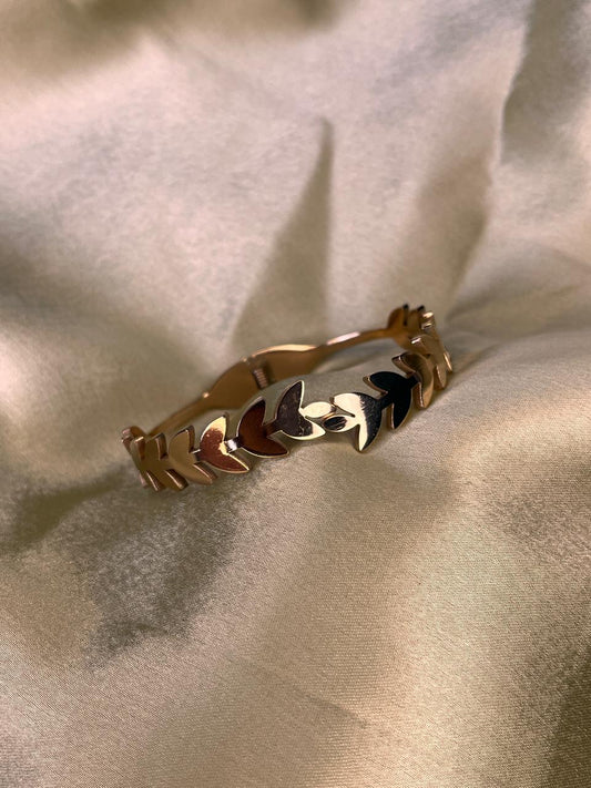 Gold bracelet with leaf designs on a beige fabric background
