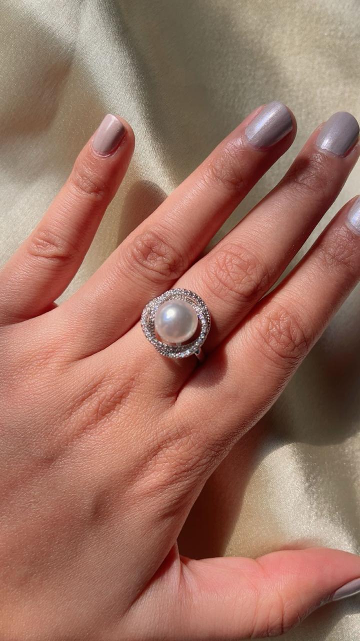 Hand wearing a ring with a pearl-like center on a neutral background