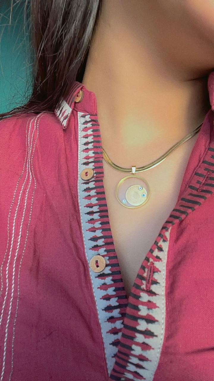 Close-up of a person wearing a pink top with a patterned collar and a necklace.