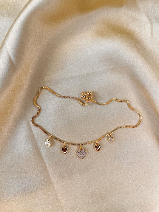 Gold anklet with heart and star charms on a beige fabric background