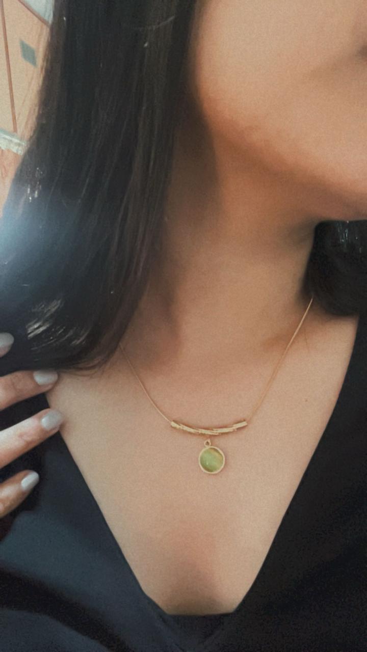 Close-up of a person wearing a gold necklace with a green pendant.