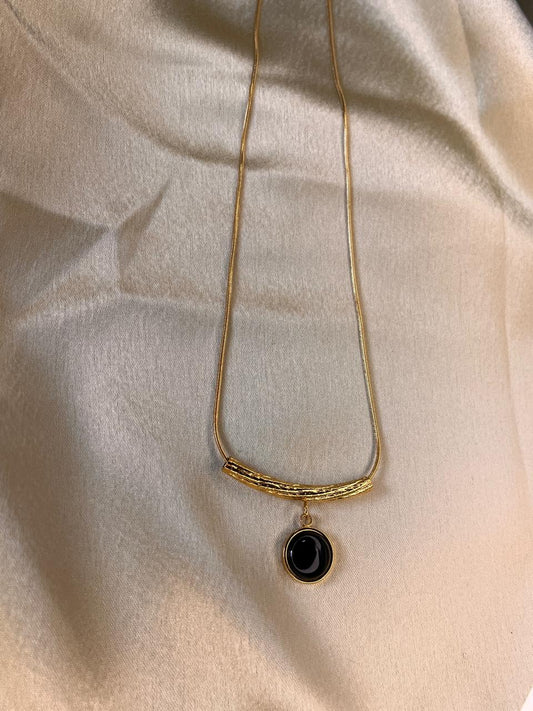 Gold necklace with a black pendant on a beige fabric background