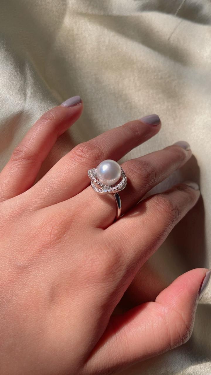 Hand wearing a pearl ring on a light fabric background