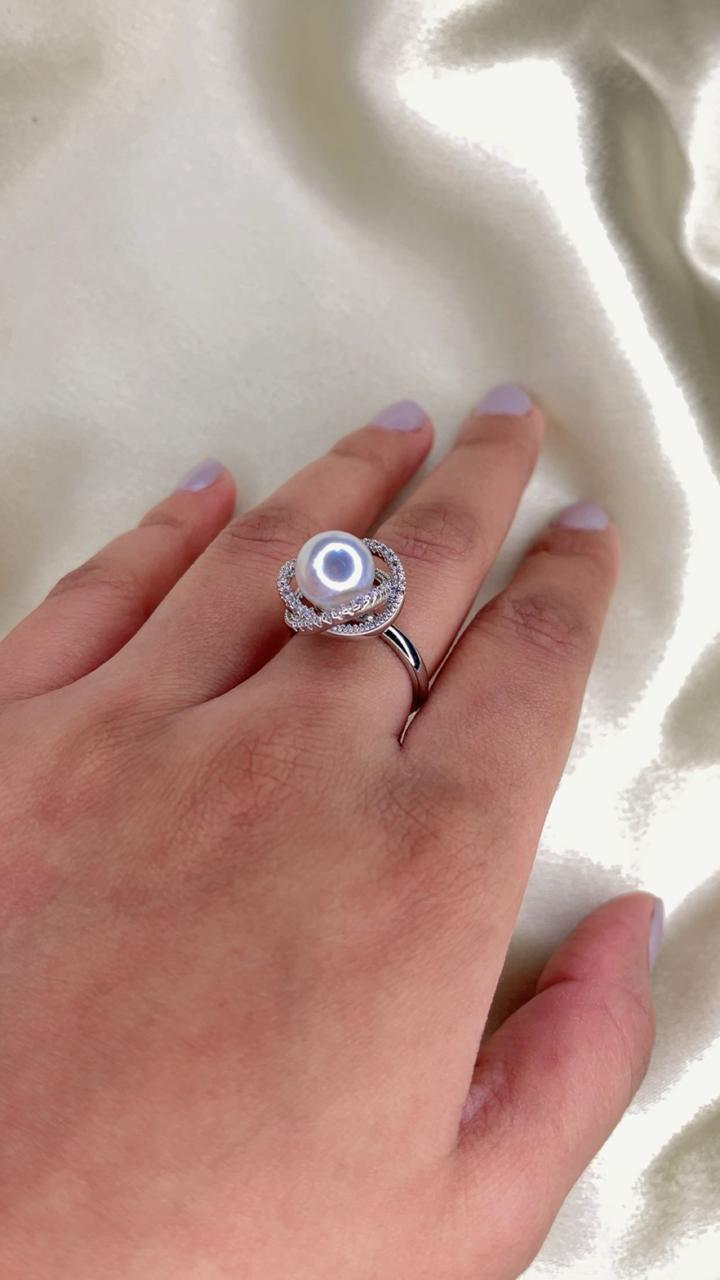 Hand wearing a silver ring with a clear gemstone on a light fabric background