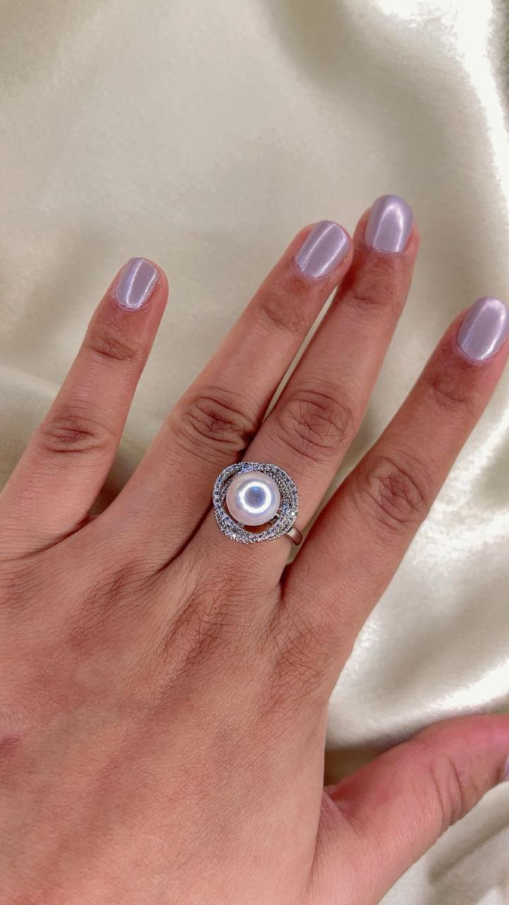 Hand wearing a silver ring with a central gemstone on a light background