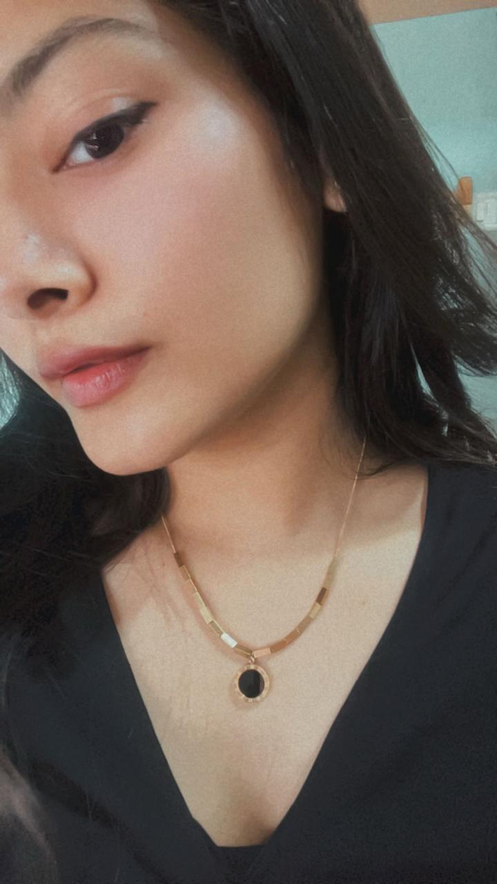 Woman wearing a gold necklace with a black pendant