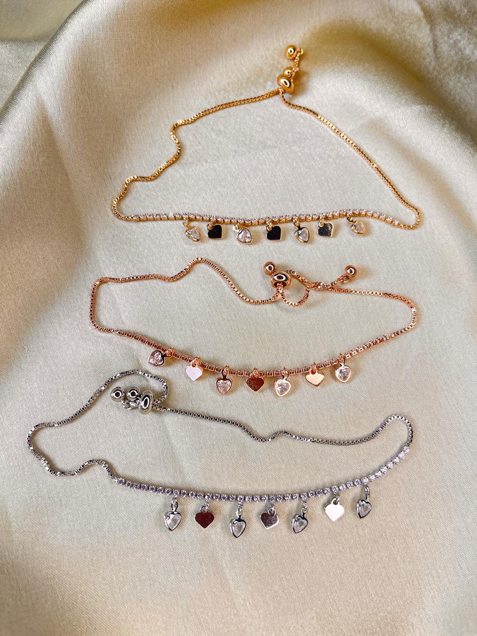 Set of three gold and rose gold necklaces with heart charms on a beige fabric background